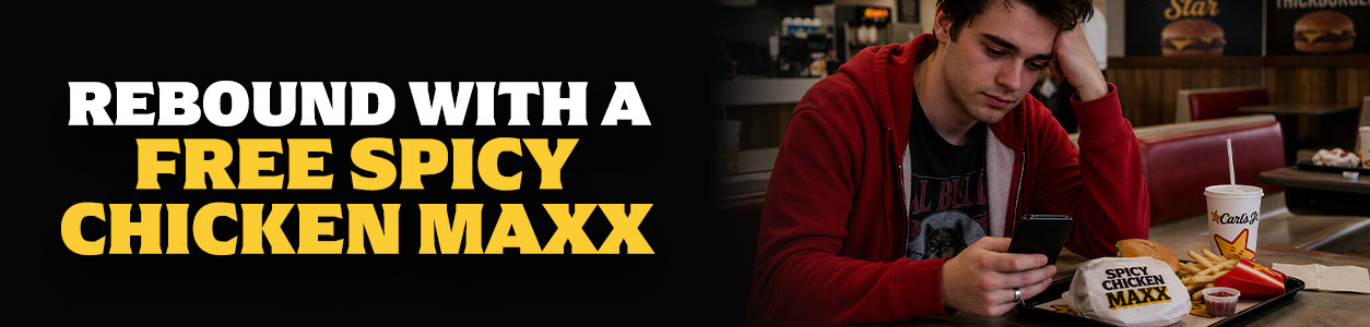 Man looking at his phone while eating a Spicy Chicken Maxx at Carl's Jr.