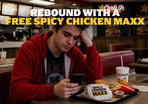 Man looking at his phone while eating a Spicy Chicken Maxx at Carl's Jr.